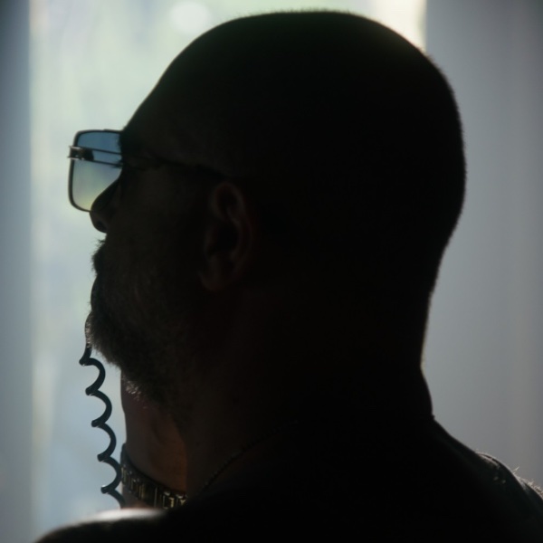Mr. Kurt in silhouette, seen from behind, wearing sunglasses, on a corded phone.