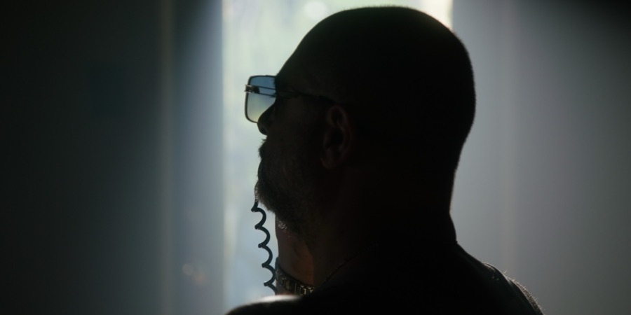 Mr. Kurt in silhouette, seen from behind, wearing sunglasses, on a corded phone.